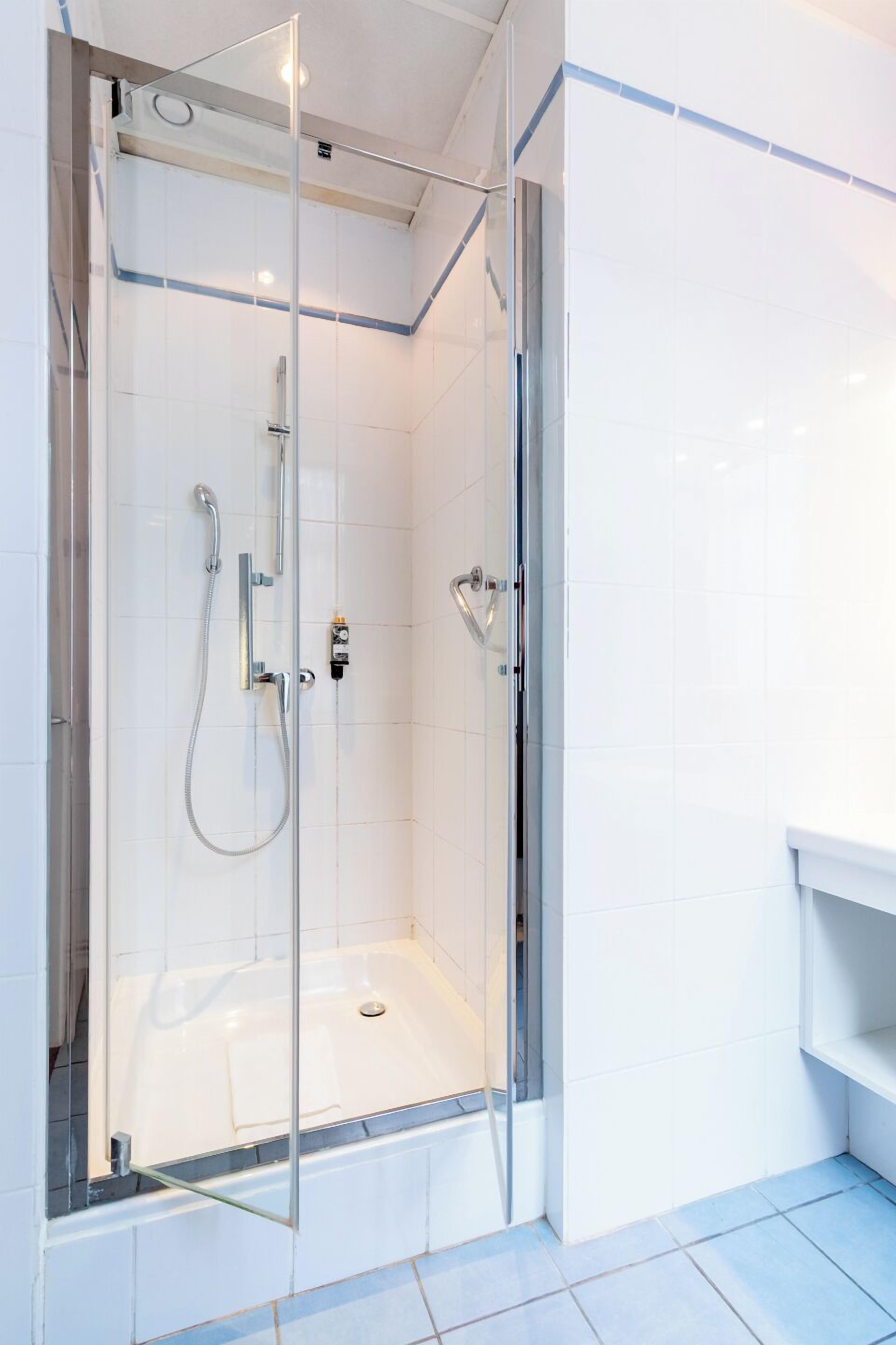 Un baño moderno con ducha envuelta en cristal, paredes cubiertas de azulejos blancos y un lavamanos blanco.