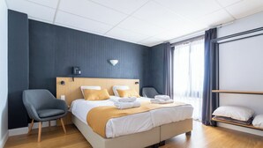 Une chambre d’hôtel moderne avec un grand lit, une table de chevet, une chaise et une étagère avec des coussins.