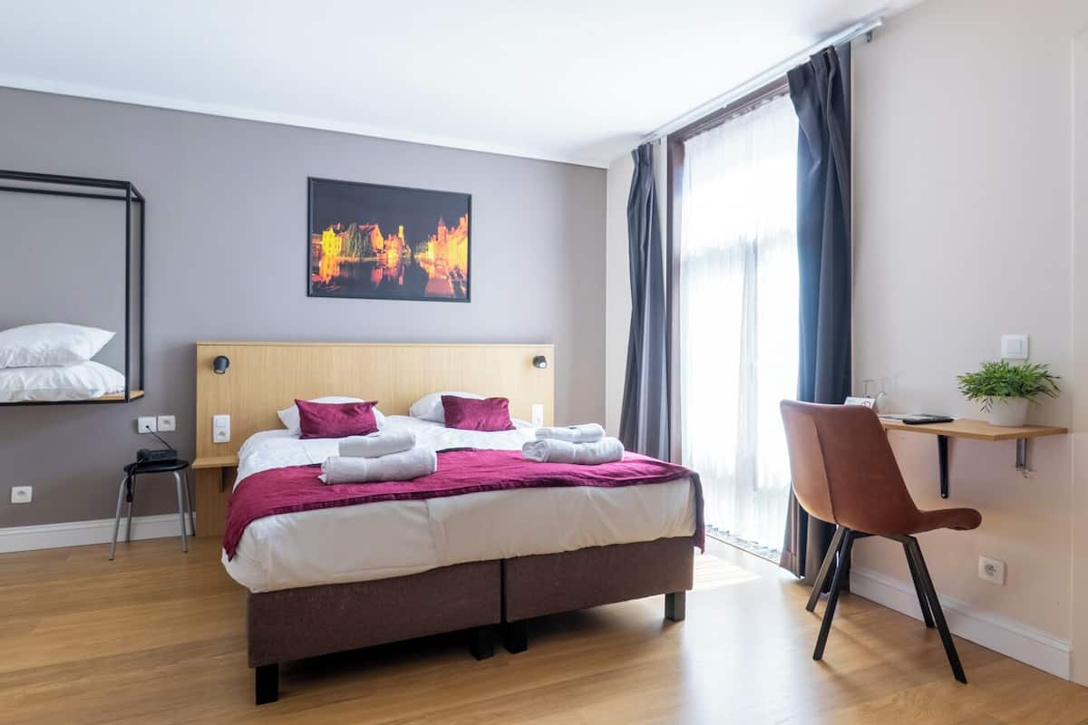 A modern hotel room with a large bed, a desk, and a chair.