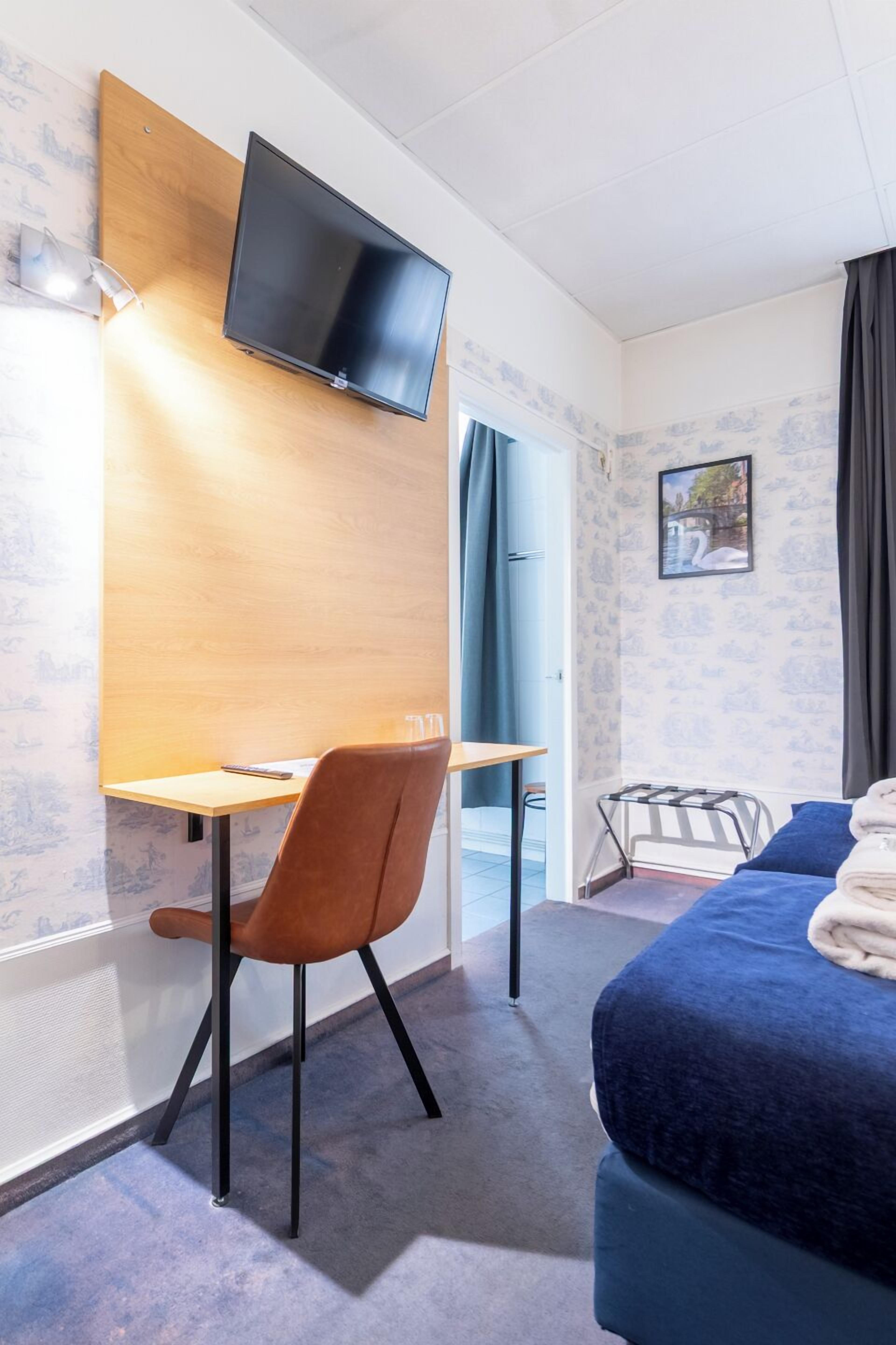 Hotellihuone, jossa on sänky, työpöytä, tuoli, seinälle asennettu televisio ja ikkuna, jossa on verhot.