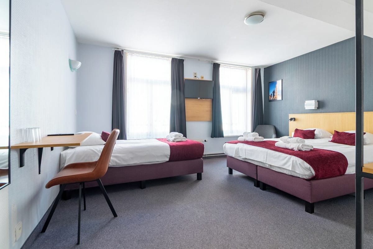 A hotel room with two beds, a desk, and a chair.
