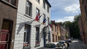 Un bâtiment doté de nombreuses fenêtres, dont certaines sont ornées de jardinières, et sur lequel on peut voir plusieurs drapeaux flottant à l’extérieur.