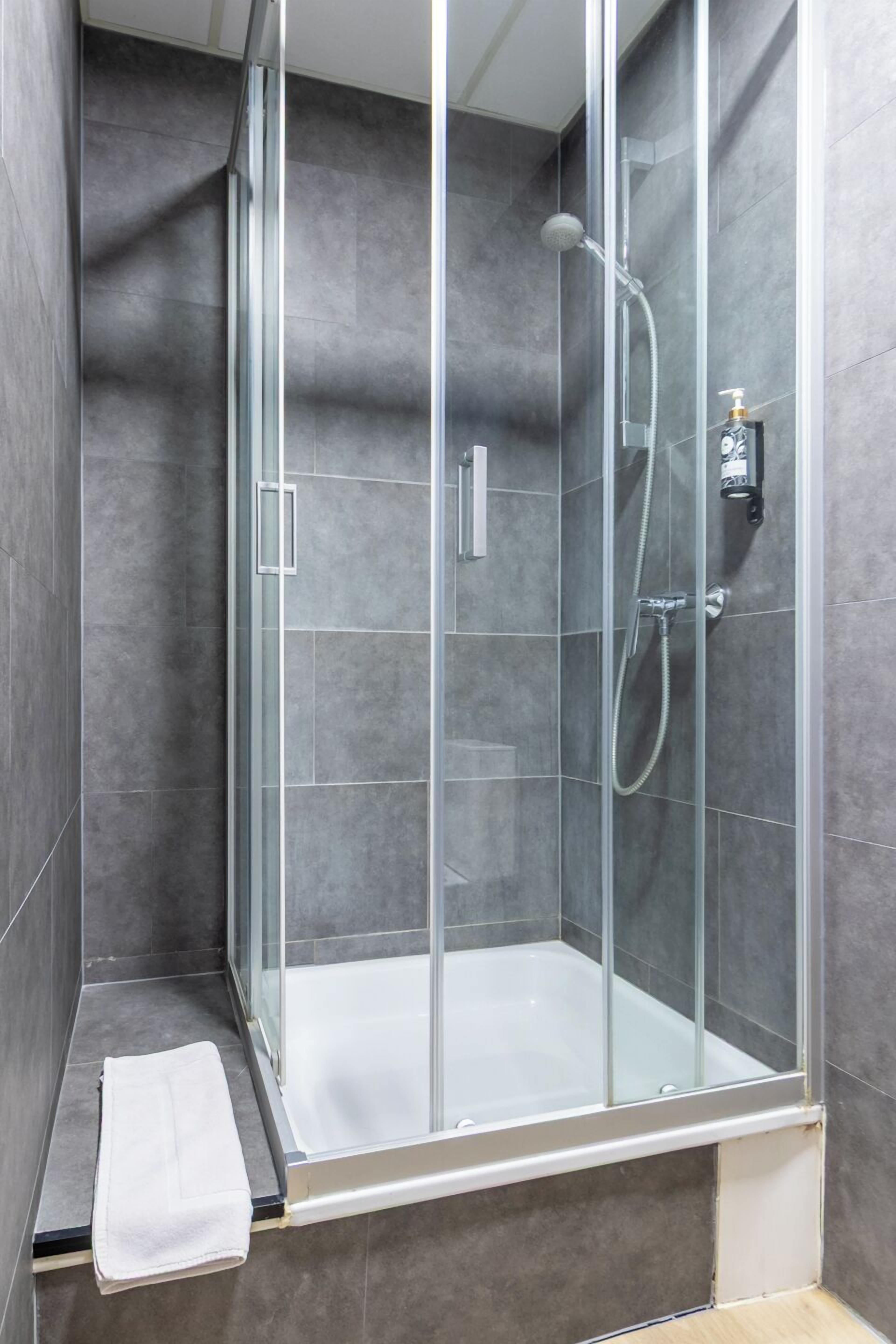 A modern shower enclosure with a glass door, a handheld showerhead, and a wall-mounted faucet.