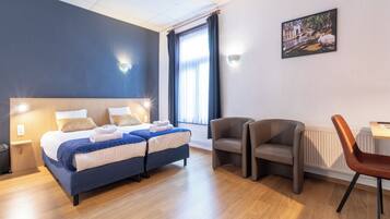 A modern hotel room with a large bed, two bedside tables, a desk with a chair, and a large window with curtains.