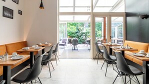 Un espace repas moderne, doté de tables et de chaises, de grandes fenêtres et offrant une vue sur l’extérieur.