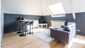 Un espace de vie compact comprenant un lit en mezzanine, un canapé, un coin repas avec une table et des chaises, et un téléviseur.