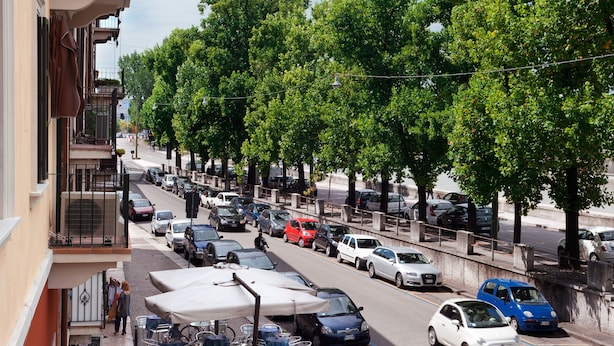 Vista d'un carrer amb cotxes aparcats, arbres i terrasses.