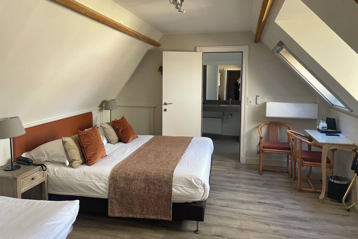 A bedroom with a bed, bedside table, lamp, and a desk with a chair.