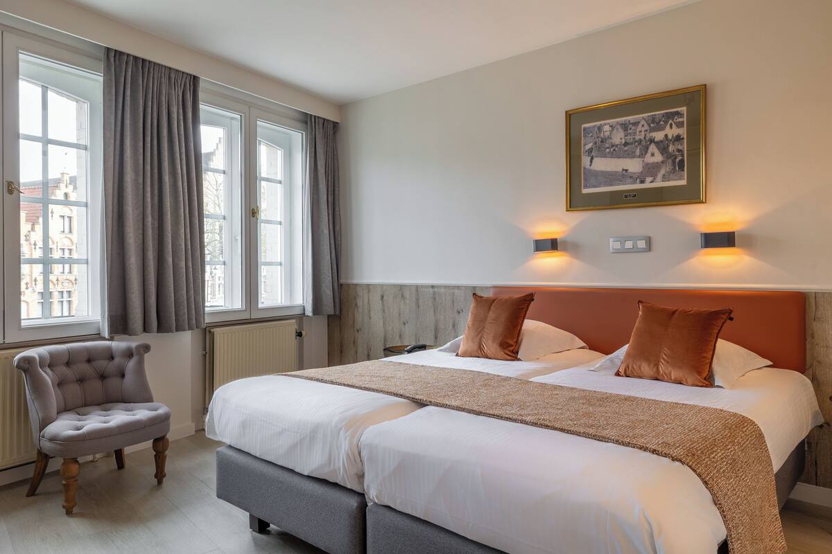 A hotel room with a large bed, a chair, a picture on the wall, and a window with curtains.