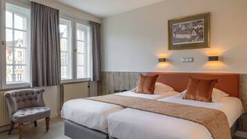 Habitación de hotel con una cama grande, una silla, un cuadro en la pared y una ventana con cortinas.