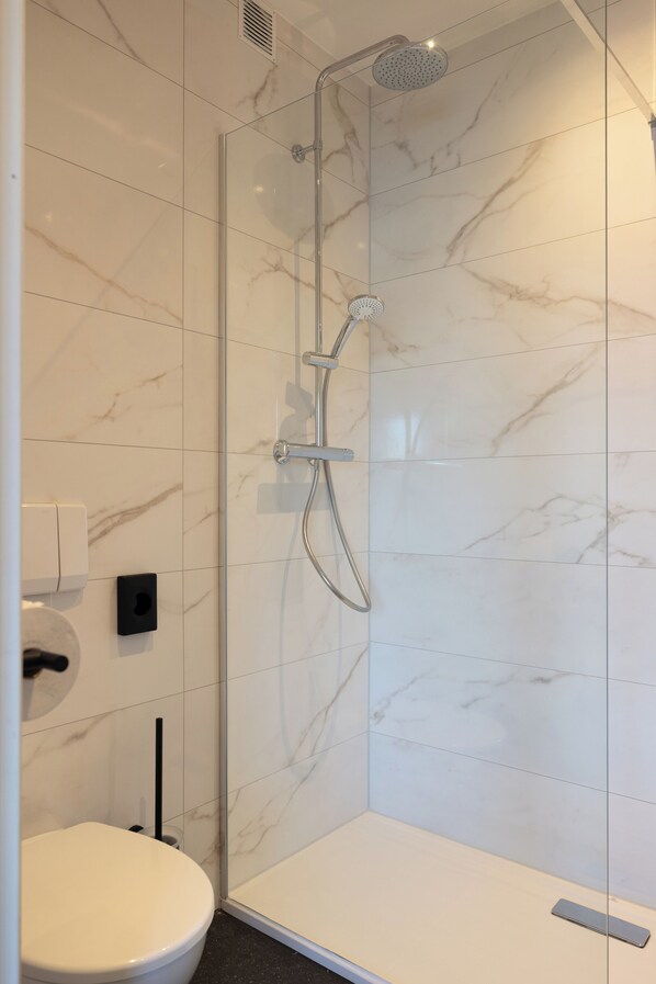 A modern bathroom with a glass-enclosed shower, white marble tiles, and a white toilet.
