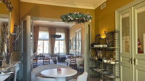 A dining area with round tables and chairs, a hanging floral arrangement, and a buffet area with shelves. - Ter Duinen (Bruges)