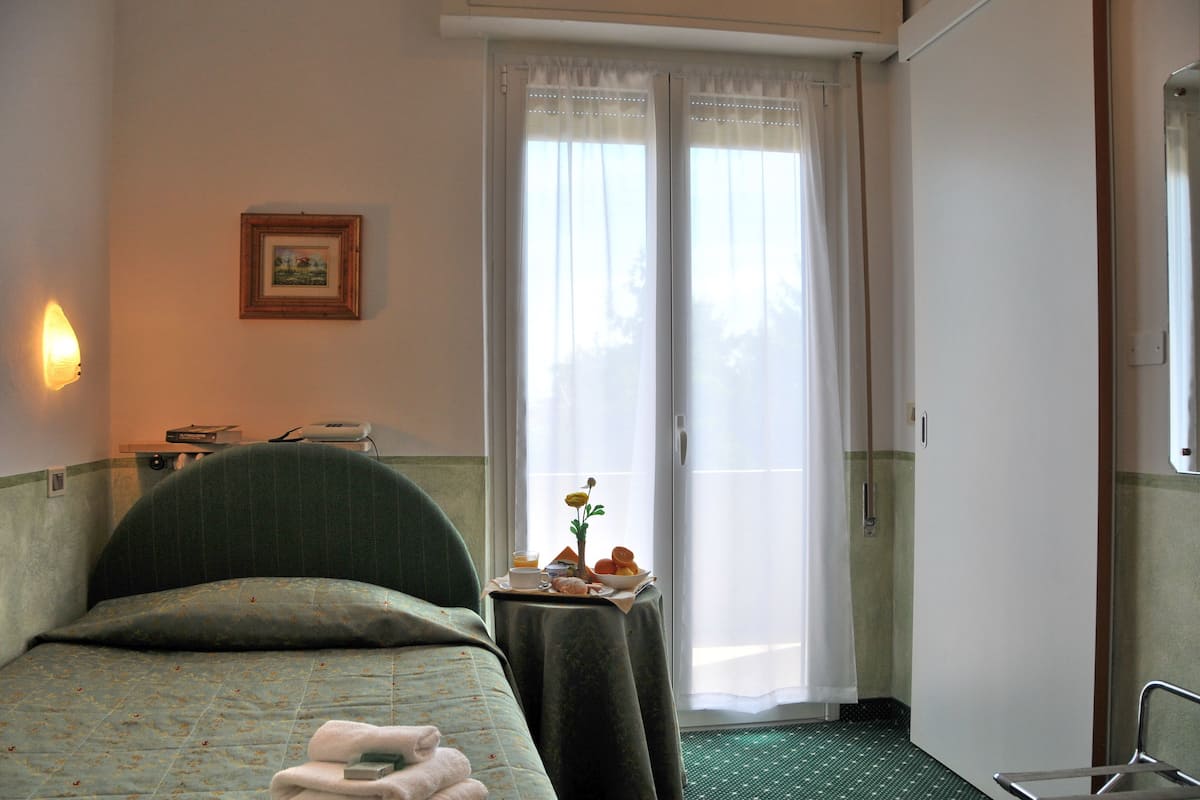 A hotel room with a bed, a small table with a tray of breakfast, a picture on the wall, and a window with curtains.