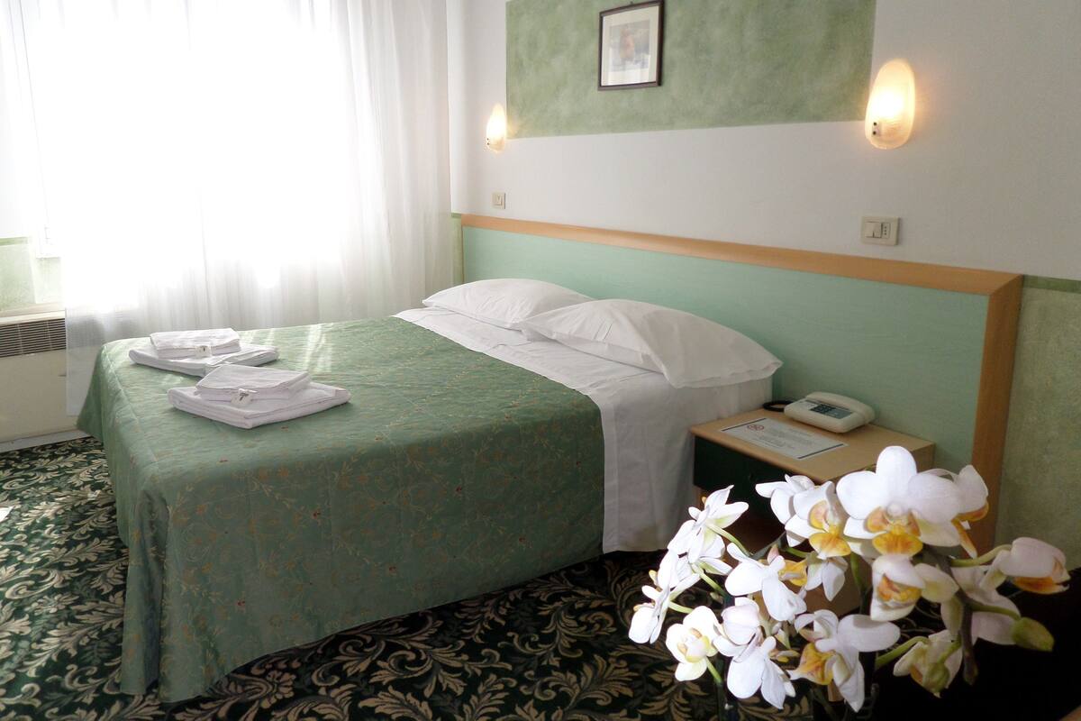 A hotel room with a bed, a nightstand, a telephone, and a picture on the wall.