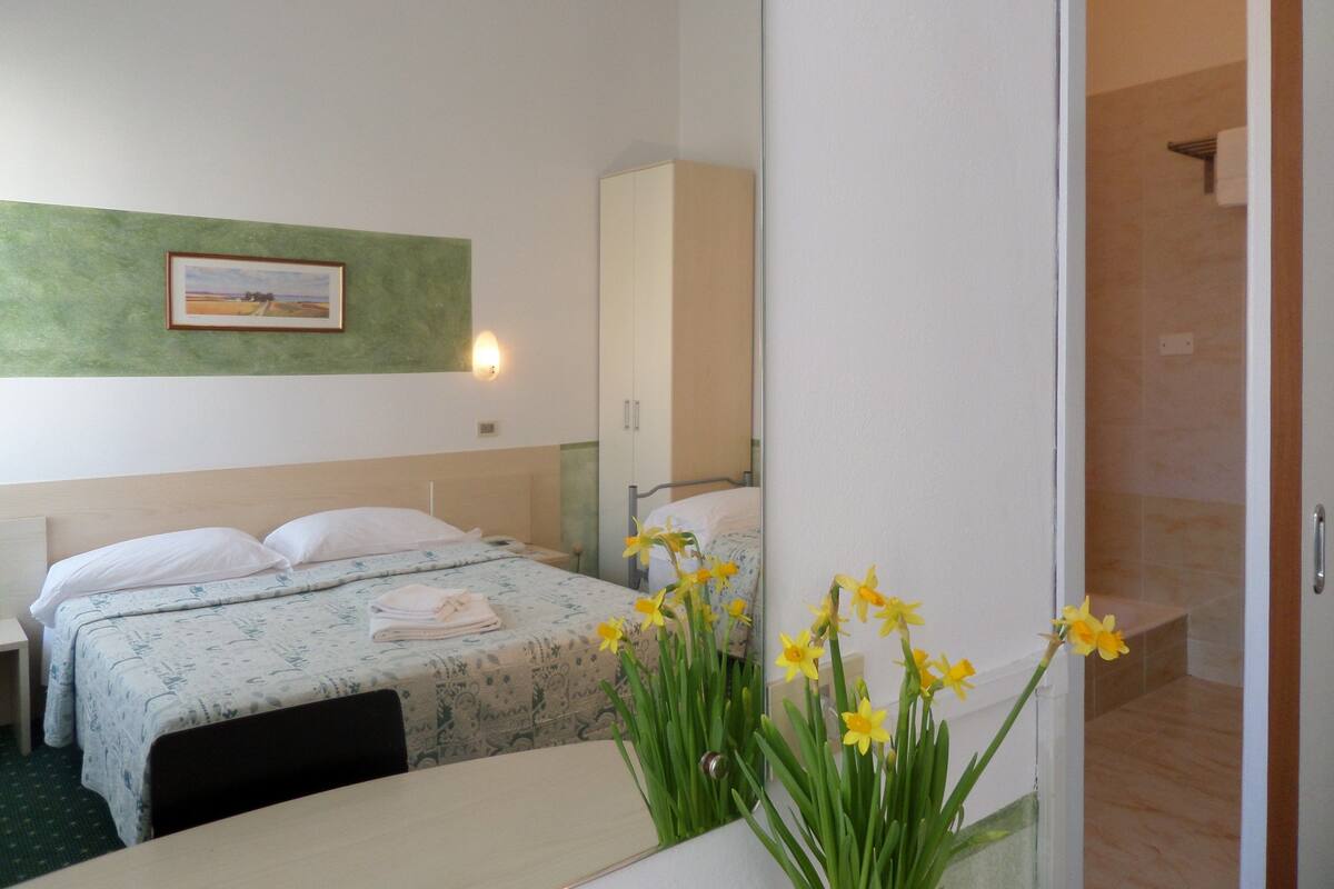 A hotel room with a bed, a bedside table, a mirror, and a wall-mounted picture.