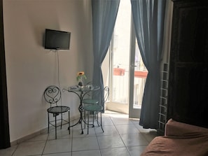 Una habitación pequeña con un televisor montado en la pared, una mesa con sillas y una ventana con cortinas.