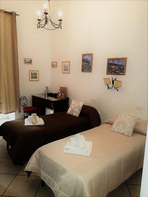 A hotel room with two beds, a desk, a chair, a chandelier, and several framed pictures on the wall. - B&B Art Suite Principe Umberto (Naples)