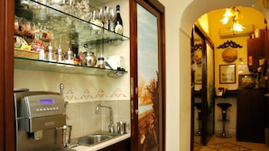 A kitchen with a coffee machine, shelves with glassware, and a tiled backsplash. - B&B Art Suite Principe Umberto (Naples)