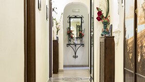 A hallway with a tiled floor, a patterned rug, a mirror, and a vase with flowers. - B&B Art Suite Principe Umberto (Naples)