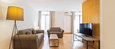 A modern living room with a sofa, armchair, coffee table, floor lamp, and a TV on a stand.