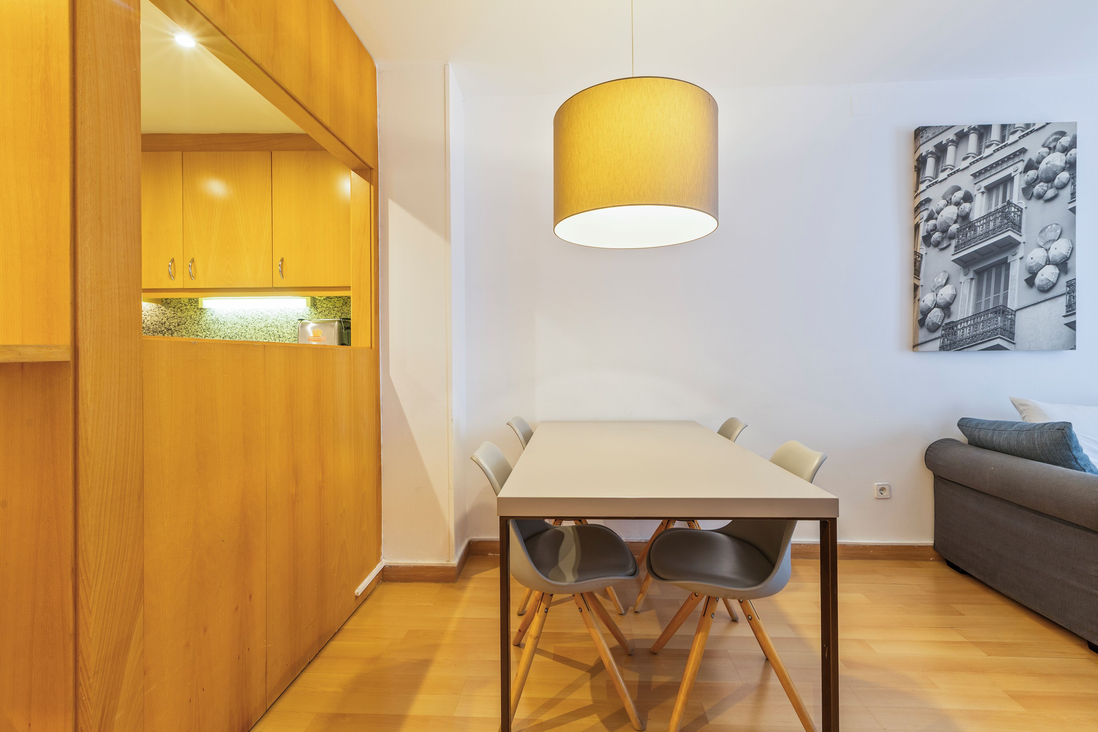 A modern kitchen with wooden cabinets, a dining table with chairs, and a pendant light.