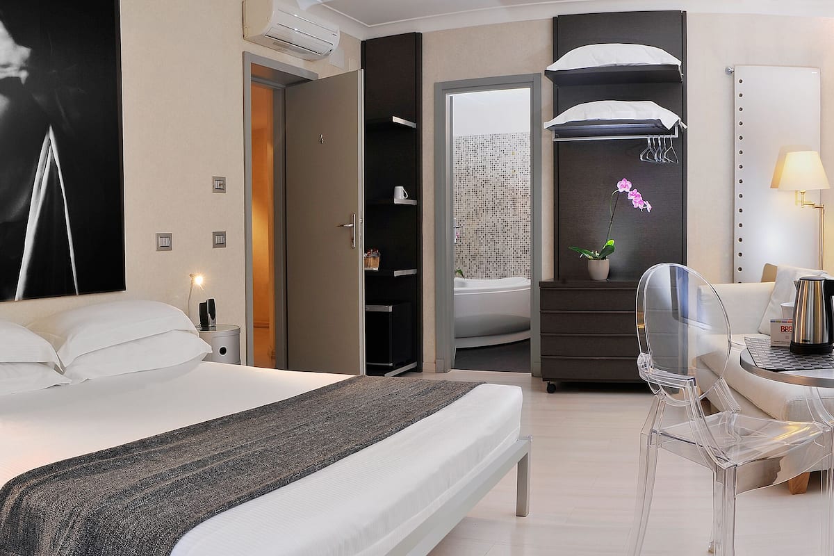 Una habitación de hotel moderna con una cama grande, un escritorio con una silla, un espejo y un baño visible a través de una puerta abierta.