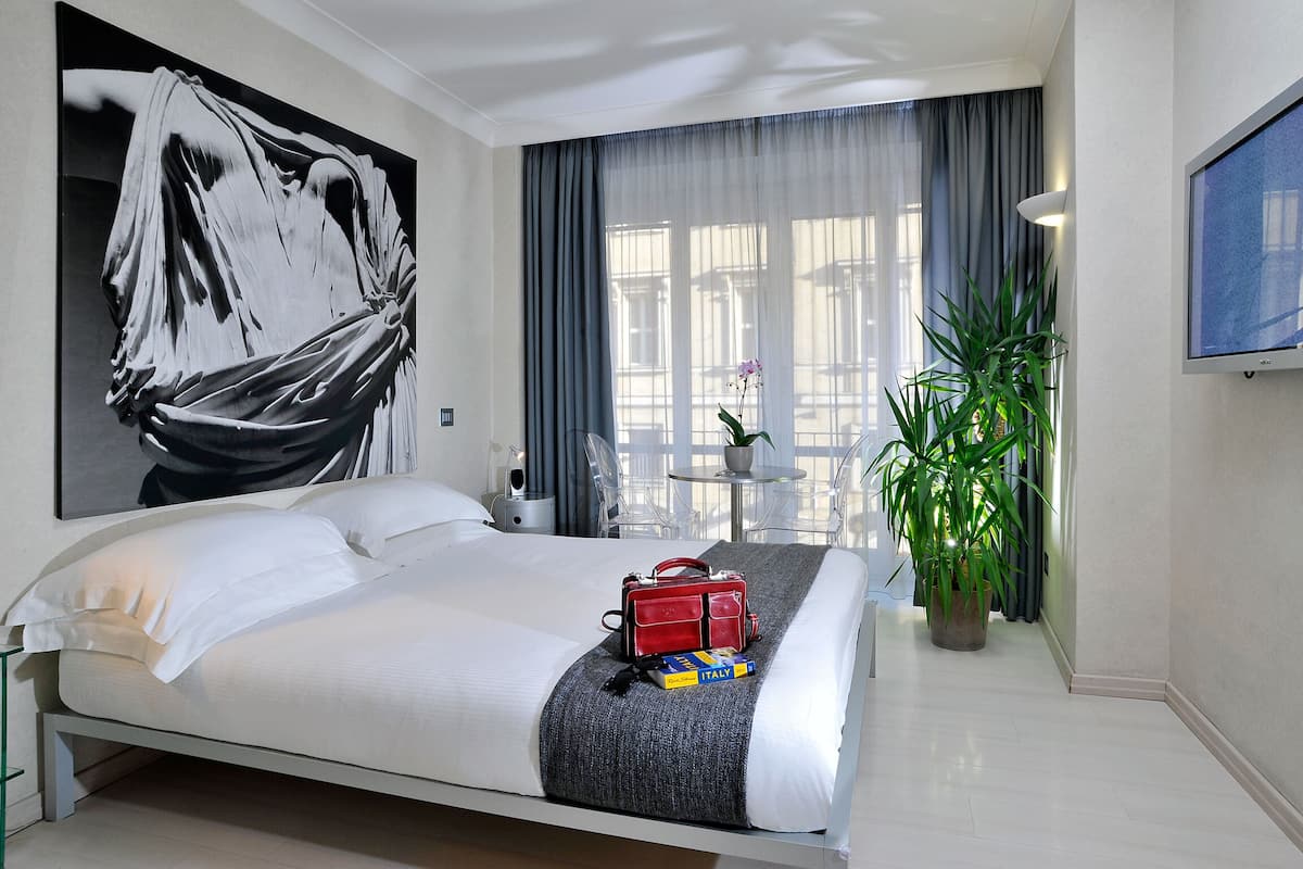 Habitación de hotel moderna con una cama grande, un bolso rojo, una planta y un cuadro en la pared.