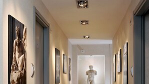 A hallway with a marble statue, framed artwork on the walls, and recessed lighting. - Best Pantheon B&B (Rome)
