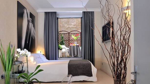 A modern hotel room with a large bed, a view of the outdoors, a potted plant, and a TV on the wall. - Best Pantheon B&B (Rome)