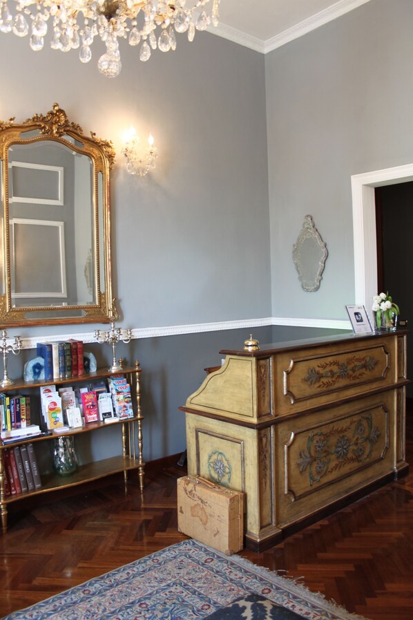 A room with a large ornate mirror, a wooden dresser, a bookshelf with books, and a chandelier. - Residenza Vespucci (Florence)