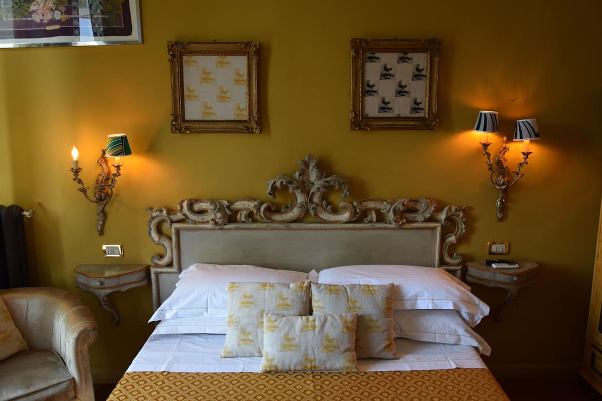 Una habitación de hotel con una cama grande, dos mesitas de noche, una silla y lámparas de pared.