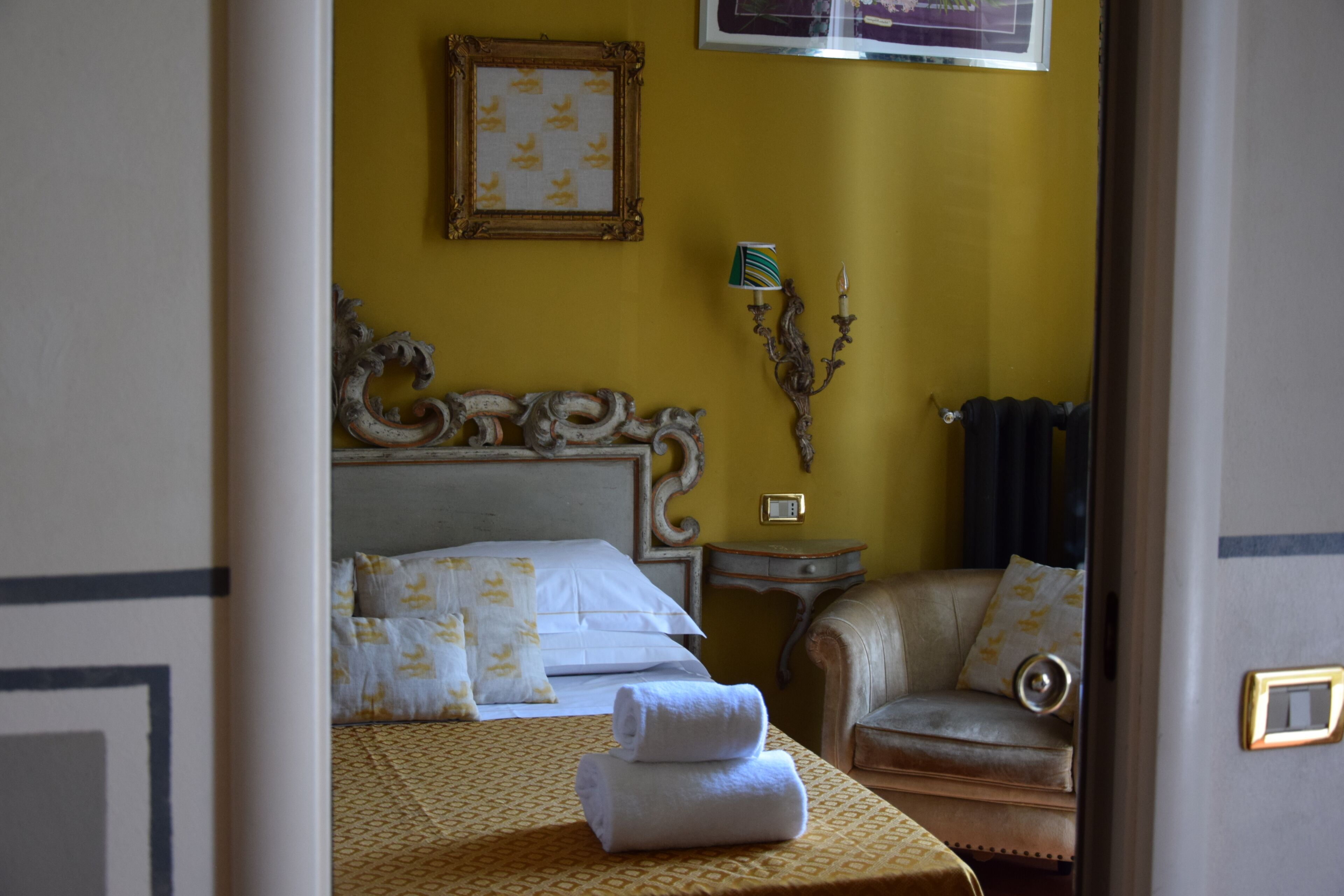 Une chambre d’hôtel avec un lit, une chaise, une table de chevet et une lampe fixée au mur.
