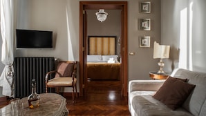 Habitación de hotel con cama, sofá, televisión, candelabro y mesa con una botella y vasos.