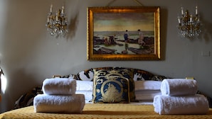 Una habitación de hotel con una cama, dos toallas, un cuadro de una playa y dos candelabros.