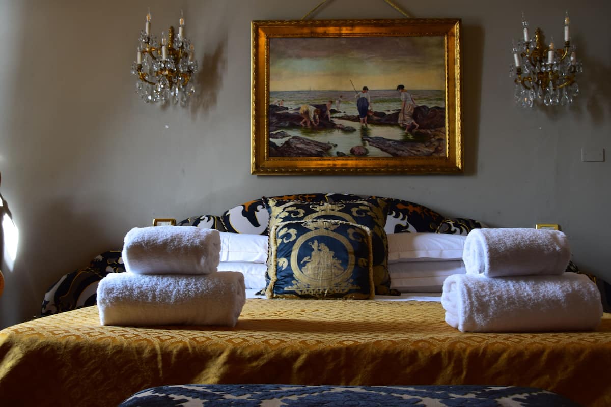 Una habitación de hotel con una cama, dos toallas, un cuadro de una playa y dos candelabros.