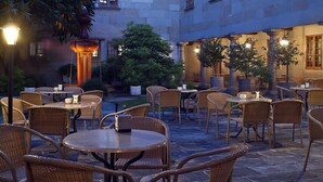 Un espace café en plein air avec des tables et des chaises en osier, un sol en pierre et un éclairage d’ambiance.
