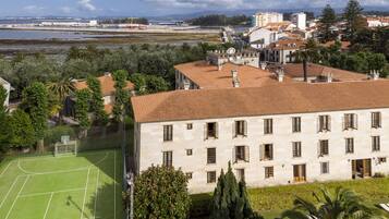 A large building with a tiled roof, surrounded by greenery and a sports field.