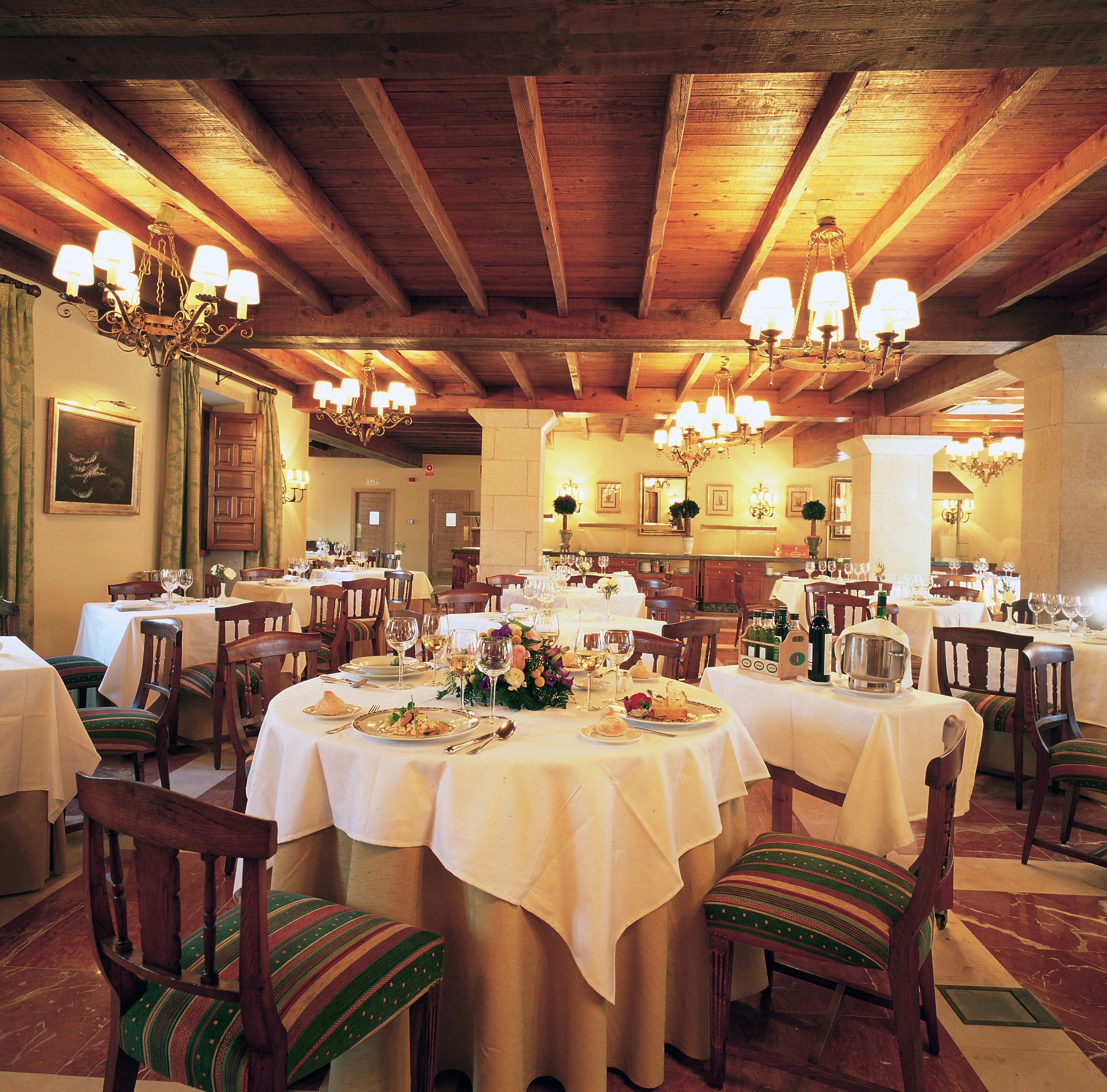 Un restaurante con vigas de madera y candelabros, mesas dispuestas con platos y copas, y sillas con cojines a rayas.