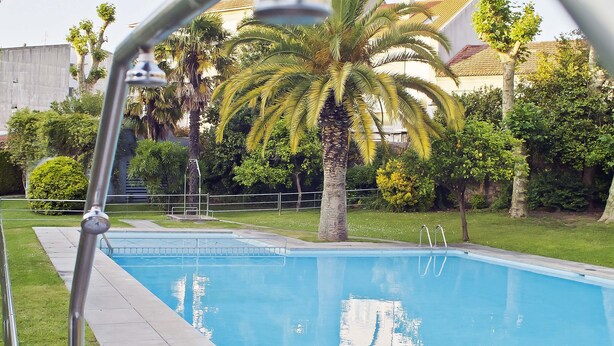 Une piscine avec un escalier en métal, entourée de verdure et avec un bâtiment en arrière-plan.