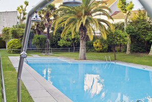 Une piscine avec un escalier en métal, entourée de verdure et avec un bâtiment en arrière-plan.
