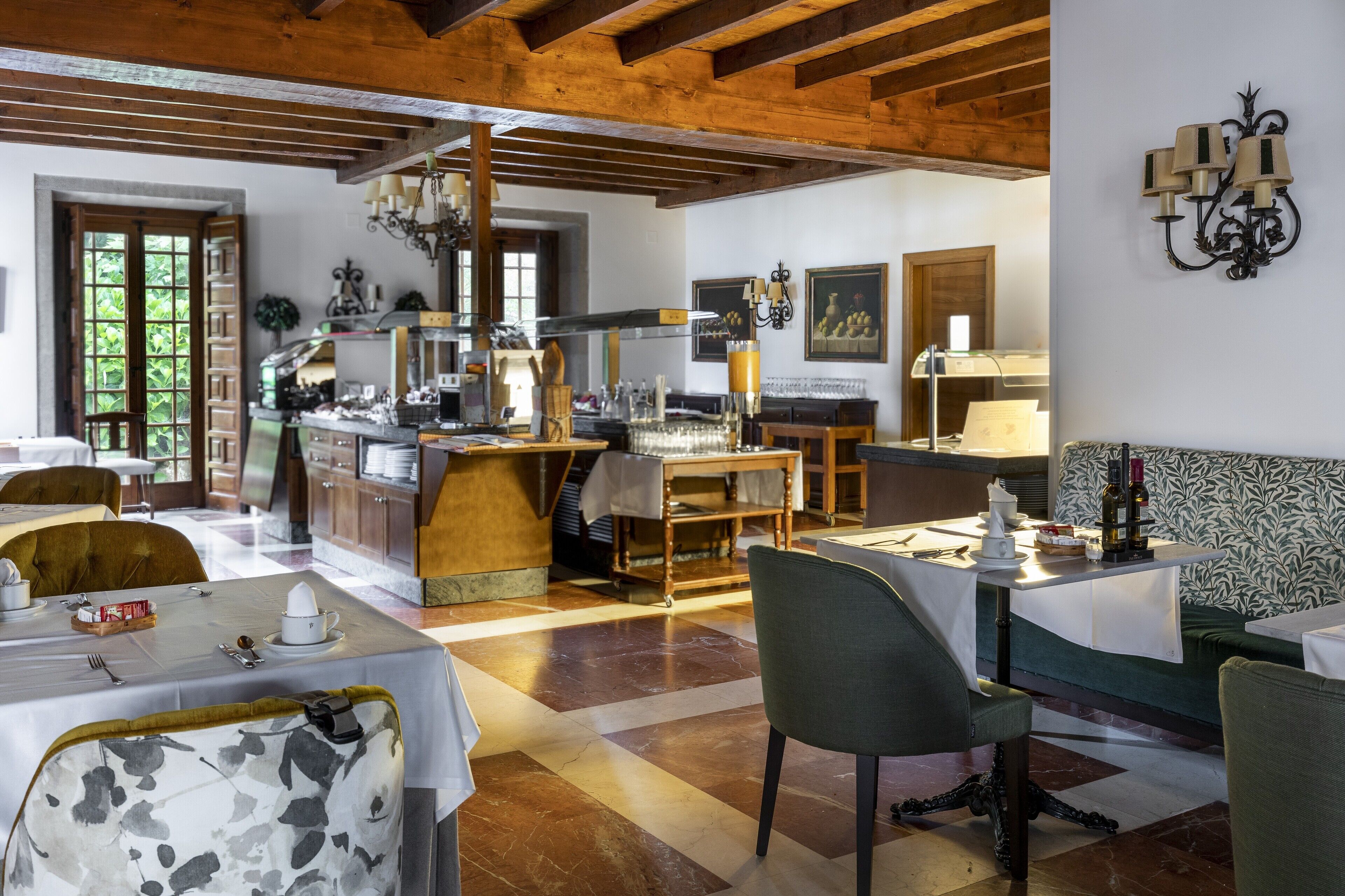 A dining area with tables set for service, a kitchen in the background, and a patterned wall.