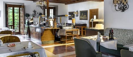 A dining area with tables set for service, a kitchen in the background, and a patterned wall.