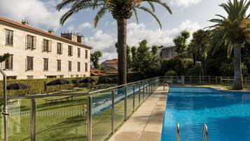 A swimming pool with a glass barrier, palm trees, and a building with multiple windows.