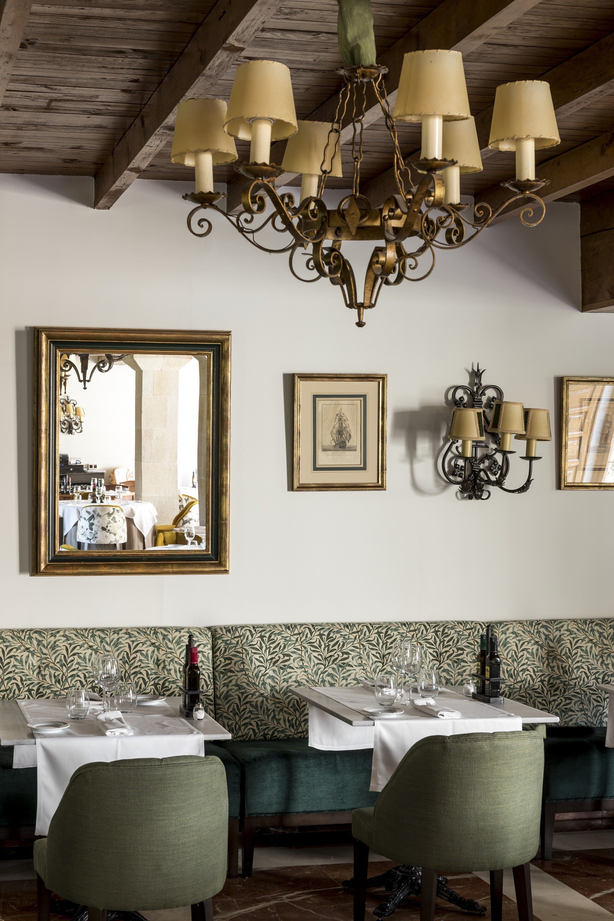 Un espace repas avec des tables préparées pour deux personnes, un lustre, des œuvres d’art encadrées et un mur orné de motifs.