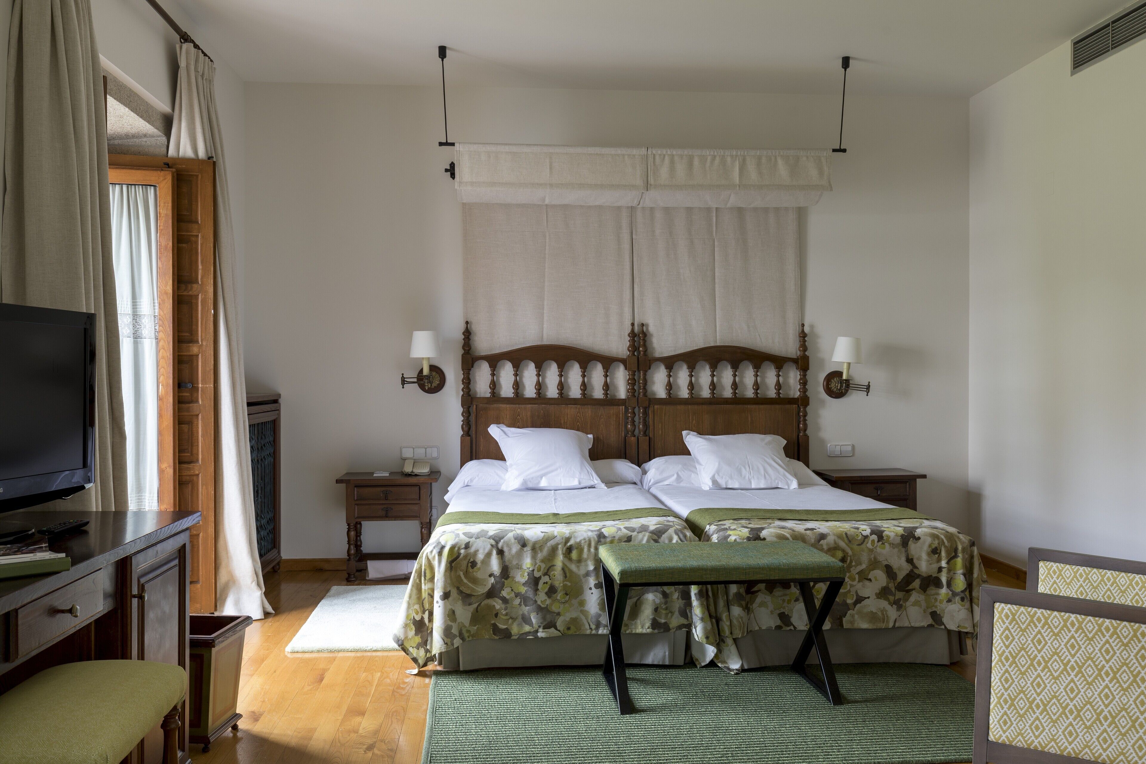 Habitación de hotel con dos camas, televisión, escritorio y ventana con cortinas.
