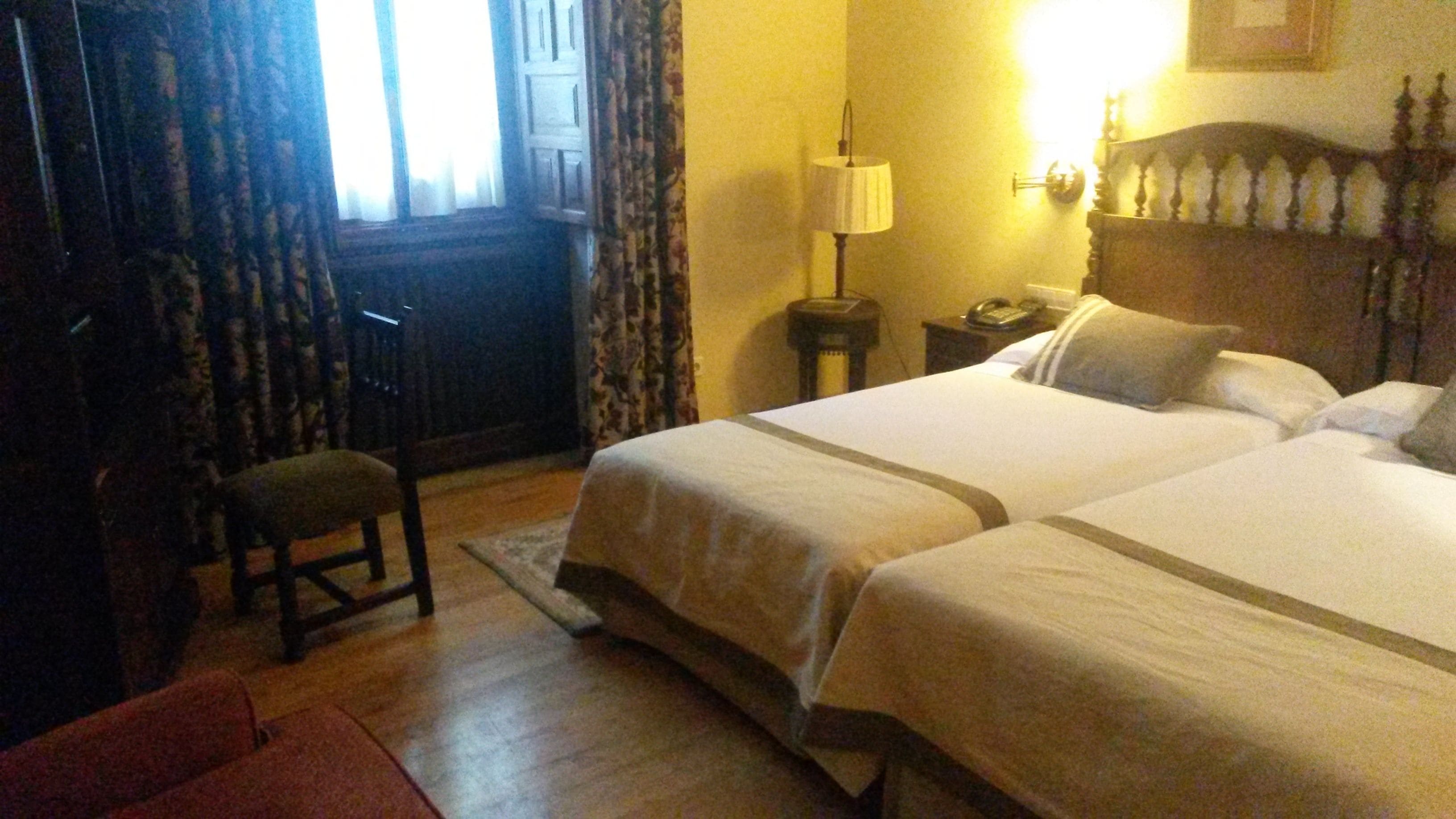 Een hotelkamer met twee bedden, een stoel, een lamp en een nachtkastje met een telefoon.