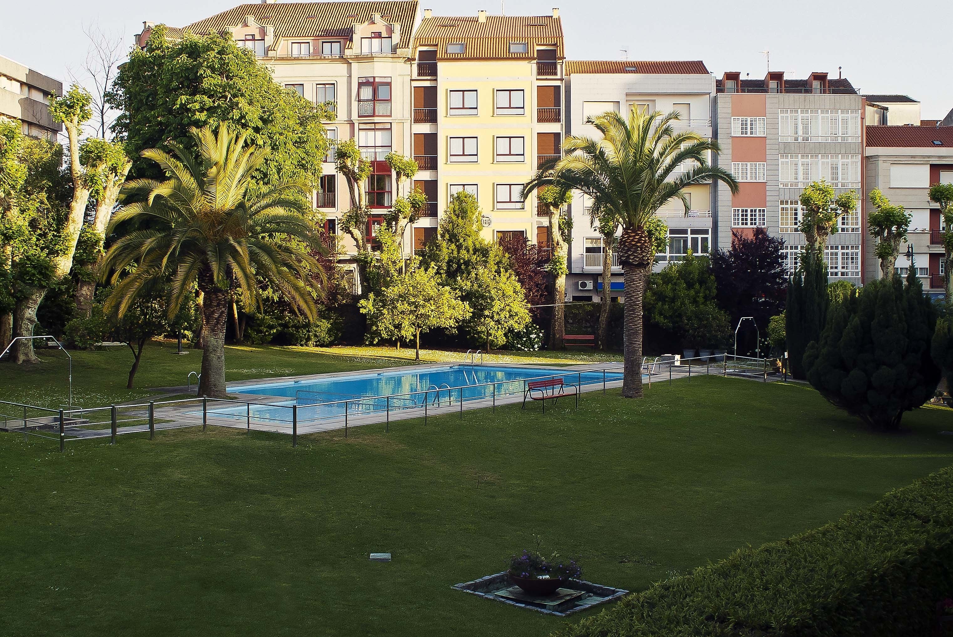 A swimming pool surrounded by well-maintained grass and palm trees, with multi-story residential buildings in the background.