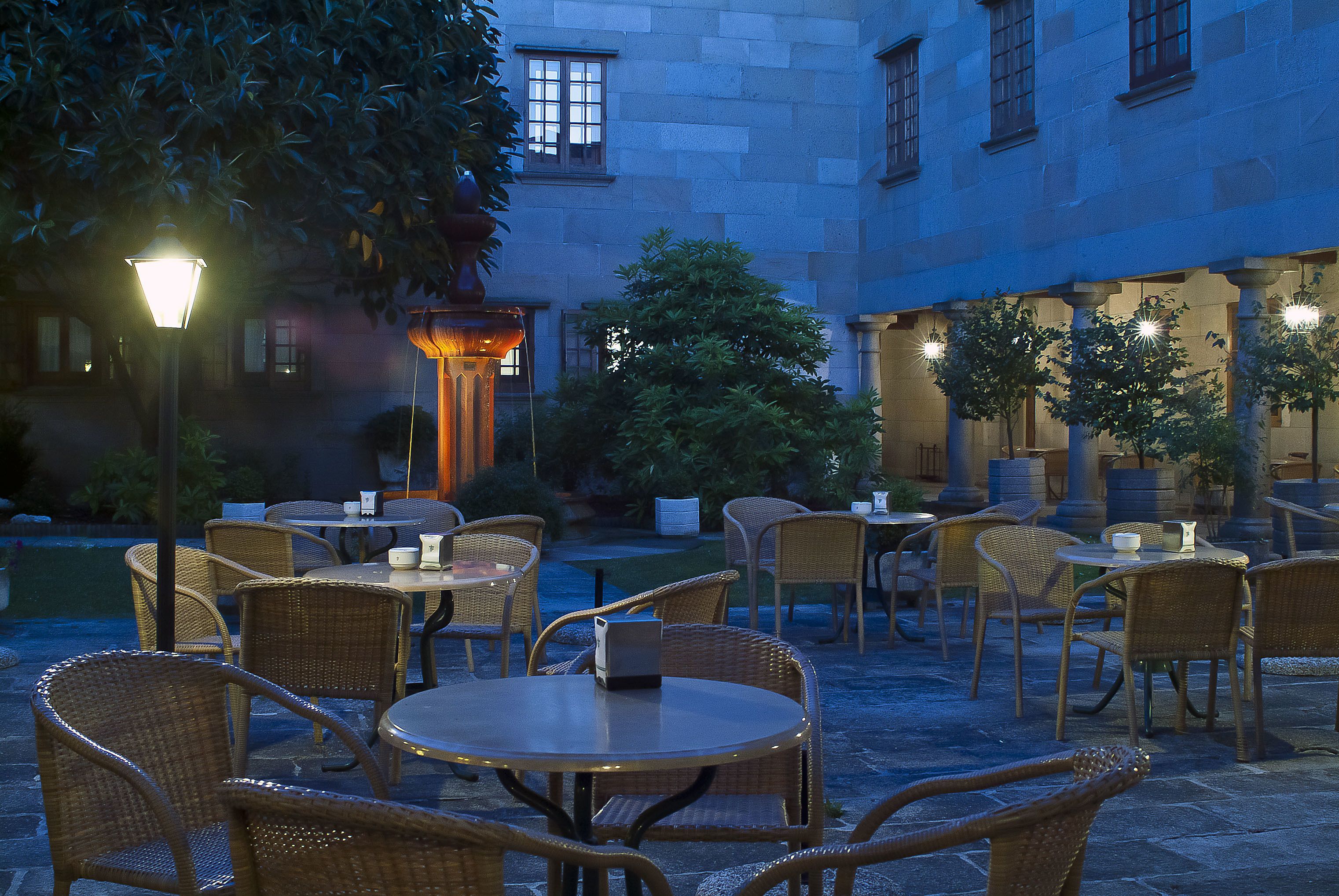 An outdoor patio area with wicker furniture and tables, surrounded by stone walls and trees.