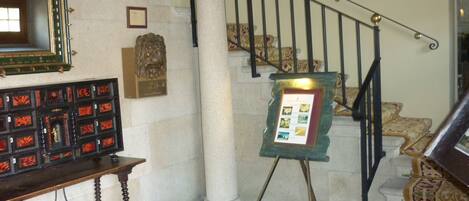 A staircase with a patterned carpet, a framed display board, and a wooden bench with a decorative mirror.