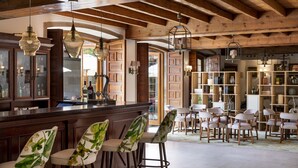 Un espace bar agrémenté de poutres en bois, de luminaires suspendus et d’un comptoir. On y trouve des tabourets de bar ainsi qu’un coin salon avec des tables et des chaises.